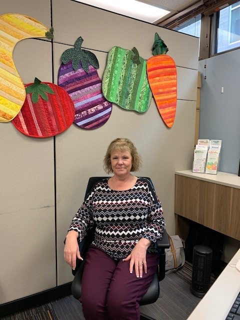 Mary sitting in a chair. Fruit and vegetables hang on wall in background.